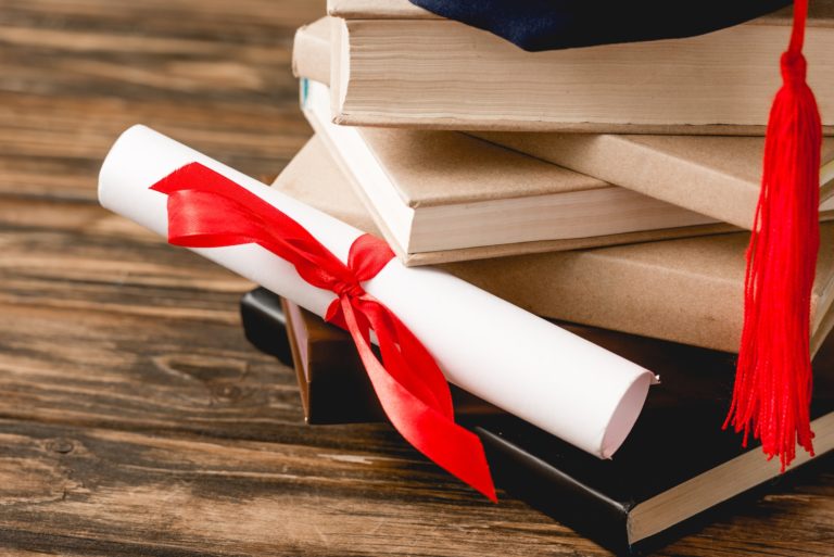 diploma with ribbon and stack of books on wooden surface